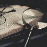 gray magnifying glass and eyeglasses on top of open book